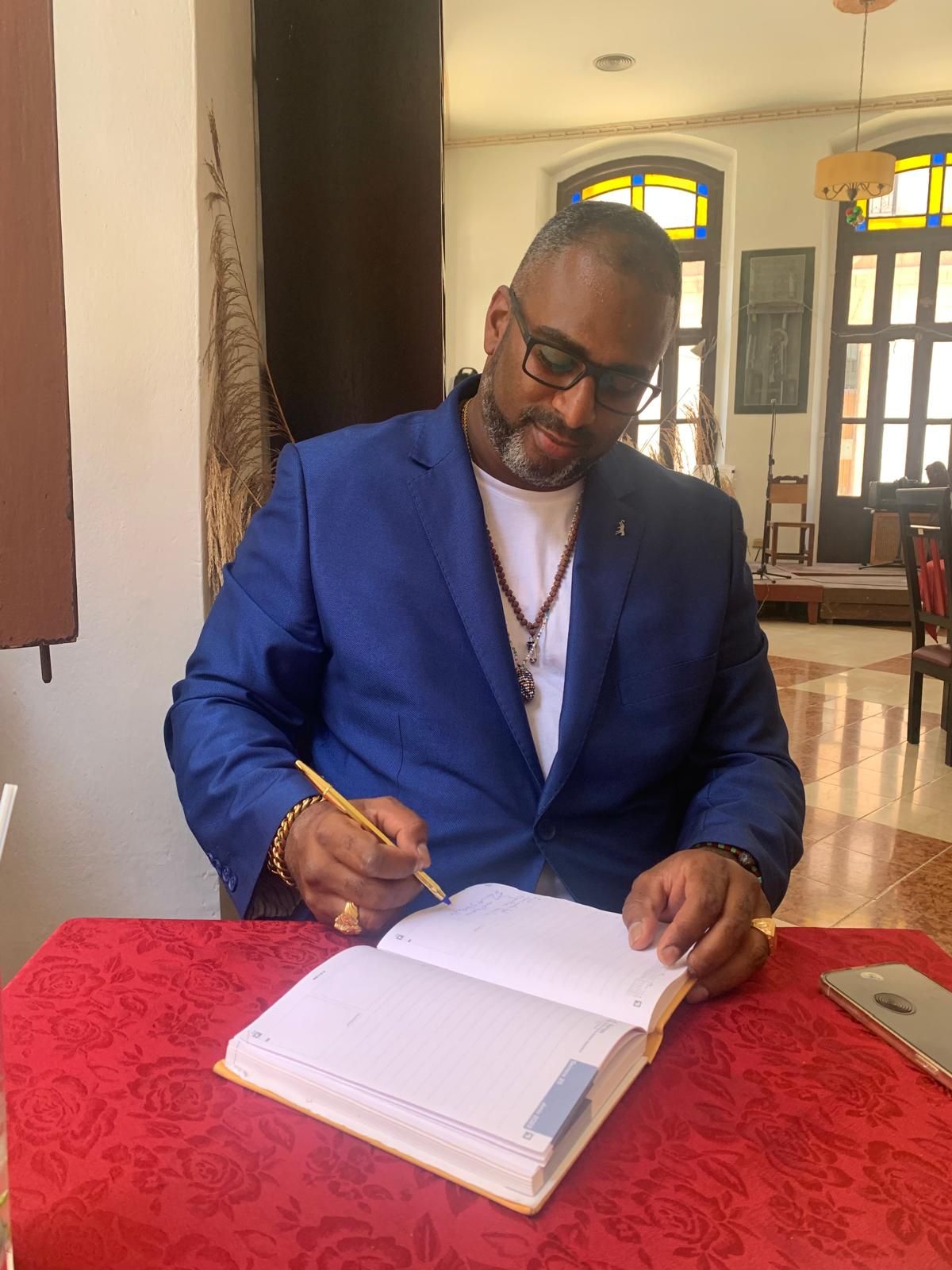 Awo Ifalade, con chaqueta azul, escribiendo en un cuaderno.